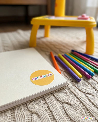 Adesivo Criativaê colado no caderno de desenho com a Table Kids ao fundo