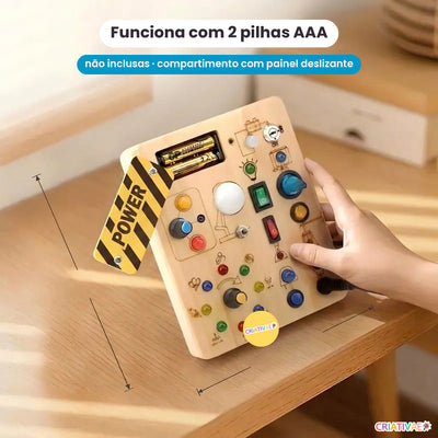 Verso do painel Busy Kids: compartimento de 2 pilhas AAA com painel deslizante